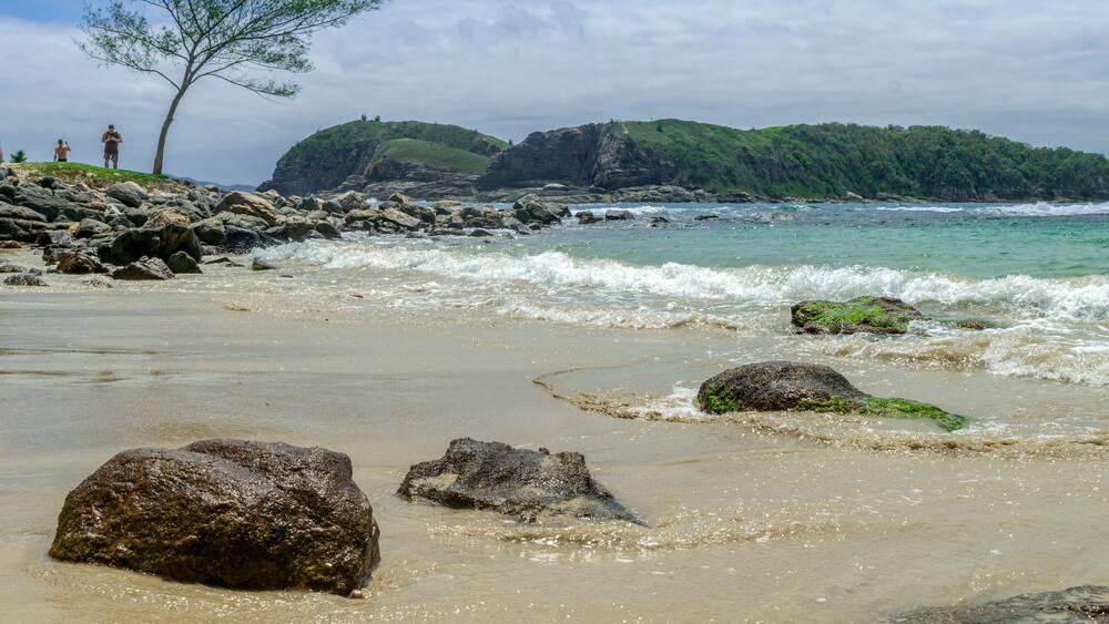 Alignment of large stones embedded in the sand, with sea and mountains in the background. Photographed on Conchas beach, Cabo Frio, Rio de Janeiro, Brazil.