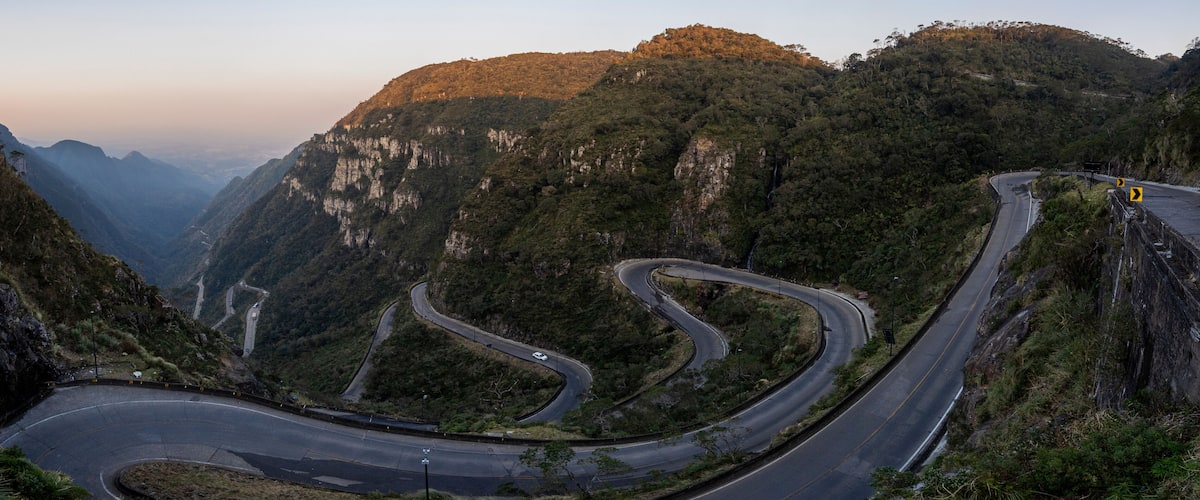 A winding mountain road with sharp bends, surrounded by lush green forests and rocky cliffs.