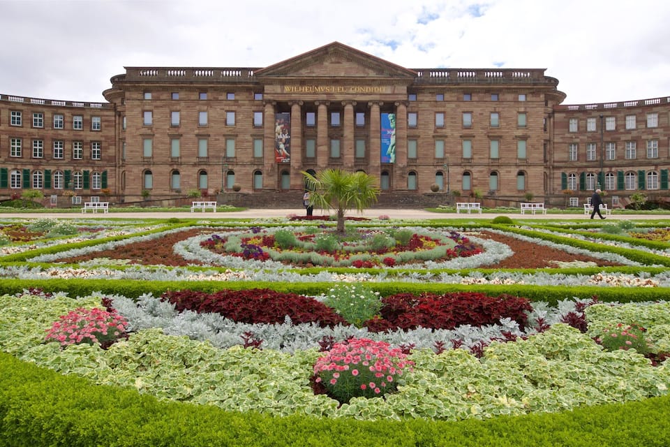 Un edifici gran amb façana clàssica i un jardí simètric al davant.