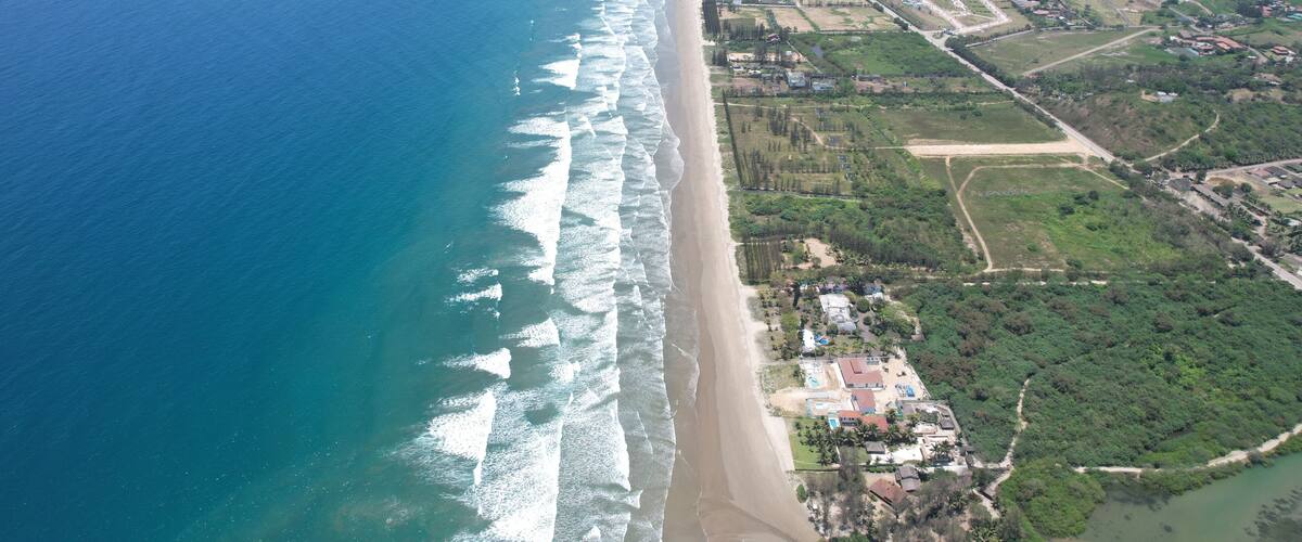 An aerial view of a coastal area with a beach, ocean, and adjacent residential and commercial buildings.