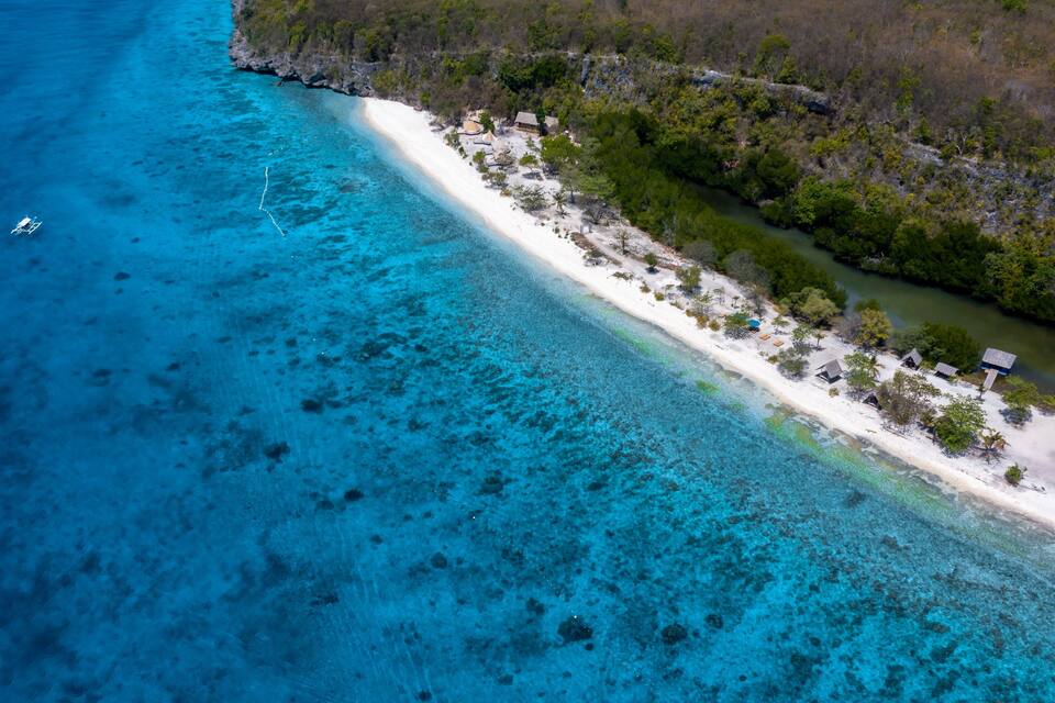 A coastal area with clear turquoise waters, a sandy beach, and scattered huts.