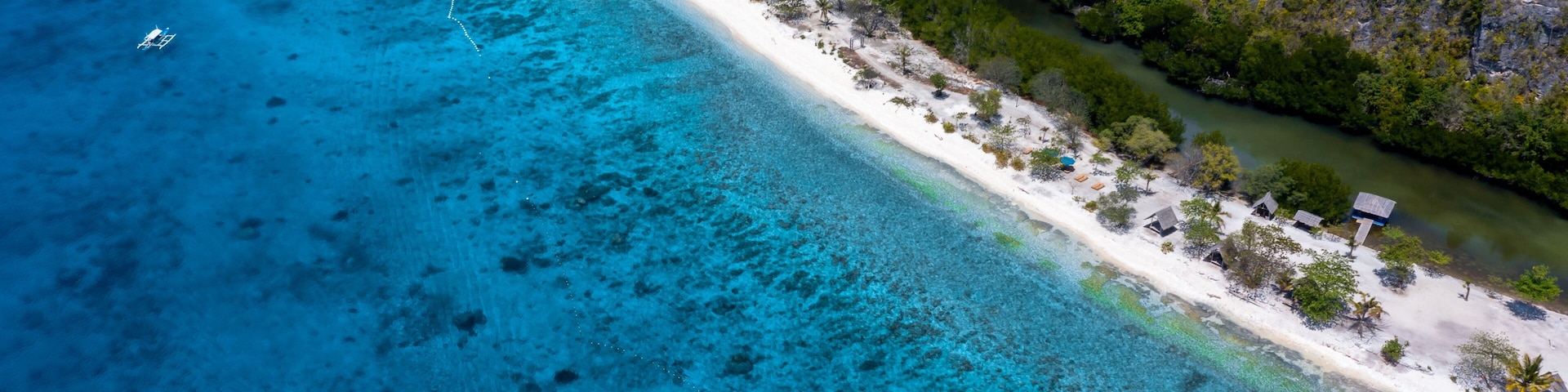 A coastal area with clear turquoise waters, a sandy beach, and scattered huts.