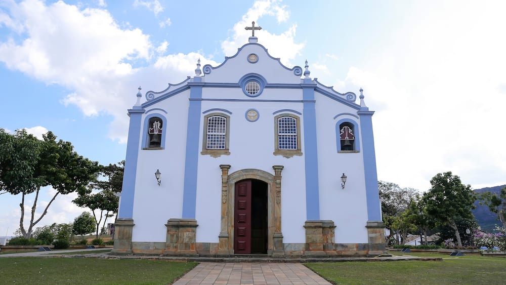Une église blanche avec une porte rouge, entourée de verdure et d’arbres.