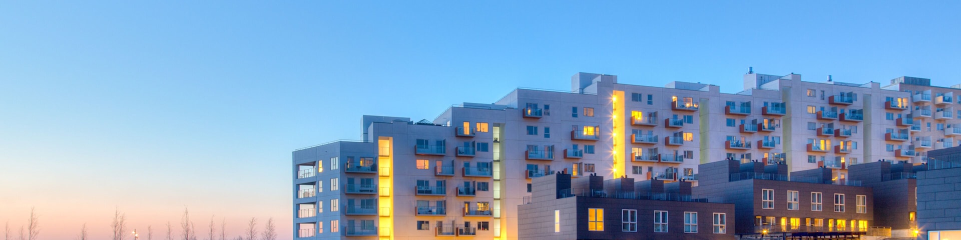 Um complexo de apartamentos moderno com água refletora na frente, sob um céu claro.