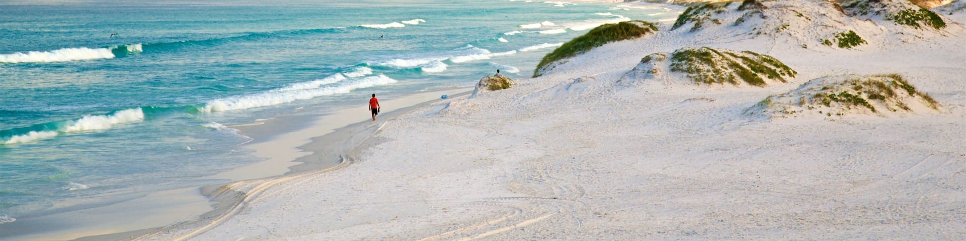 A beach with white sand, waves, and a person walking.