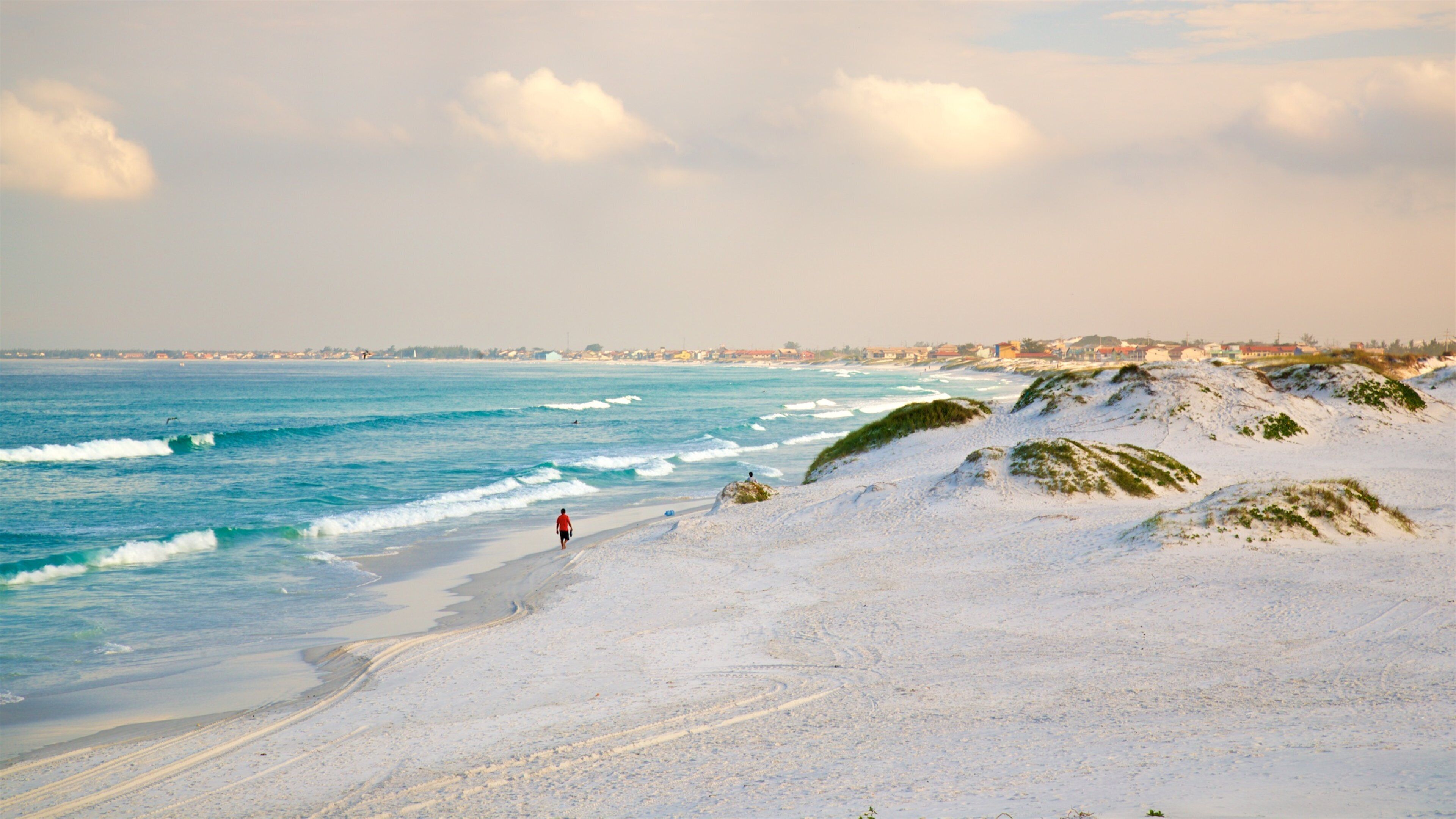 A beach with white sand, waves, and a person walking.