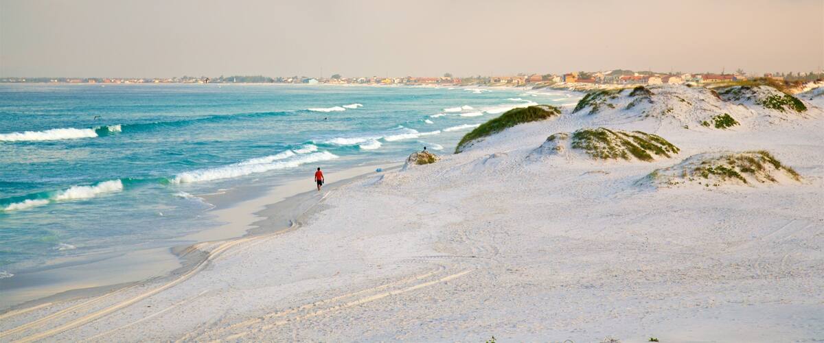 A beach with white sand, waves, and a person walking.