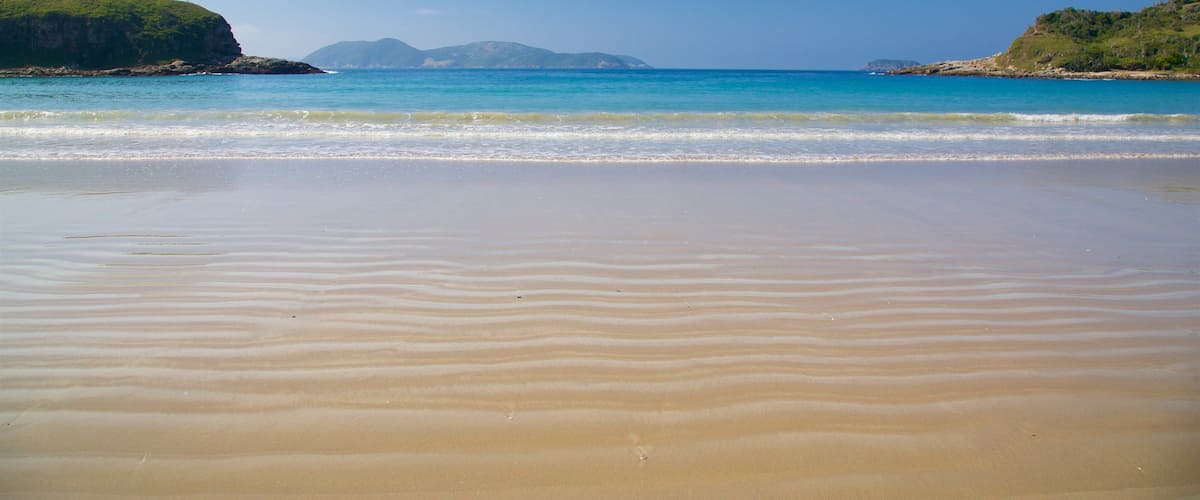 A sandy beach with gentle waves, clear blue water, and distant green hills.