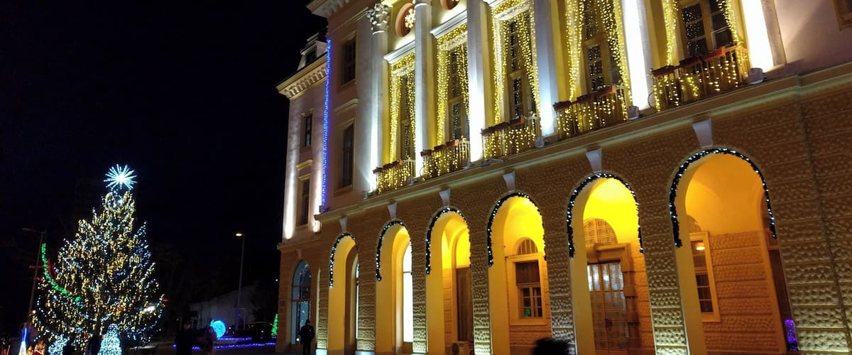 A grand building with illuminated columns and arches, a large Christmas tree, and a snowflake decoration on the roof.