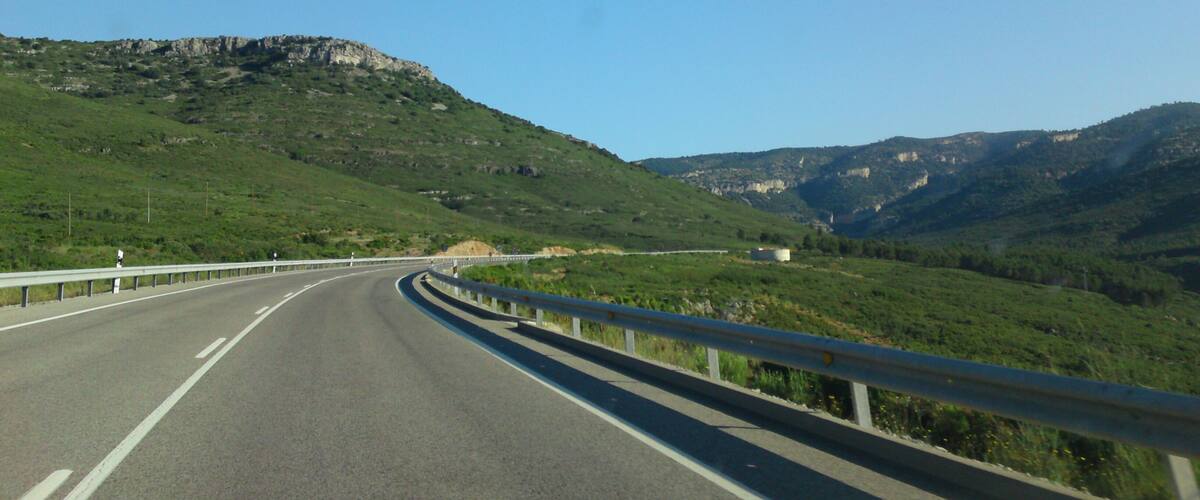 A highway curving through a mountainous landscape with green hills and rocky cliffs.