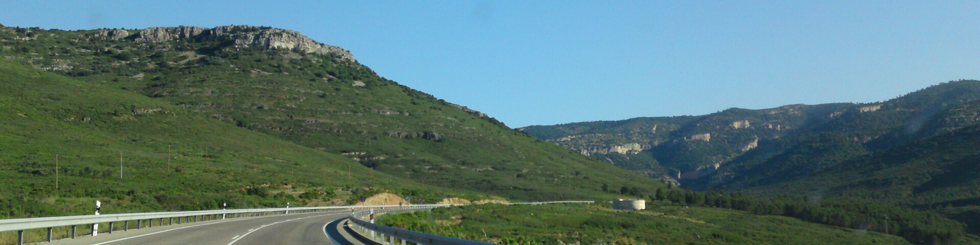 A highway curving through a mountainous landscape with green hills and rocky cliffs.