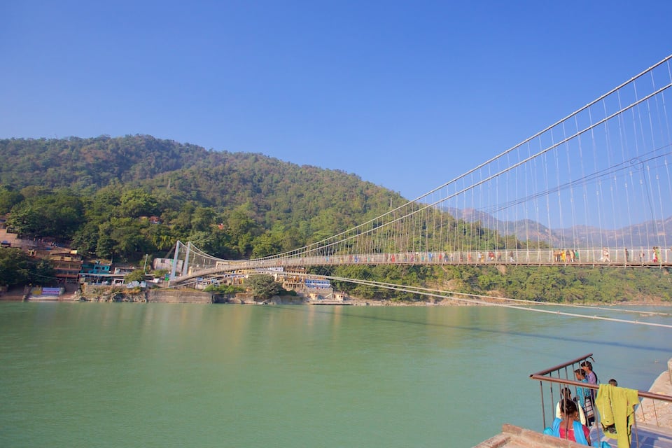A suspension bridge over a river with a forested hillside in the background.