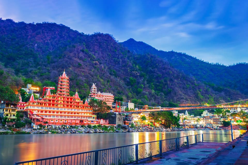 A river with a bridge, a temple complex, and a mountainous backdrop.