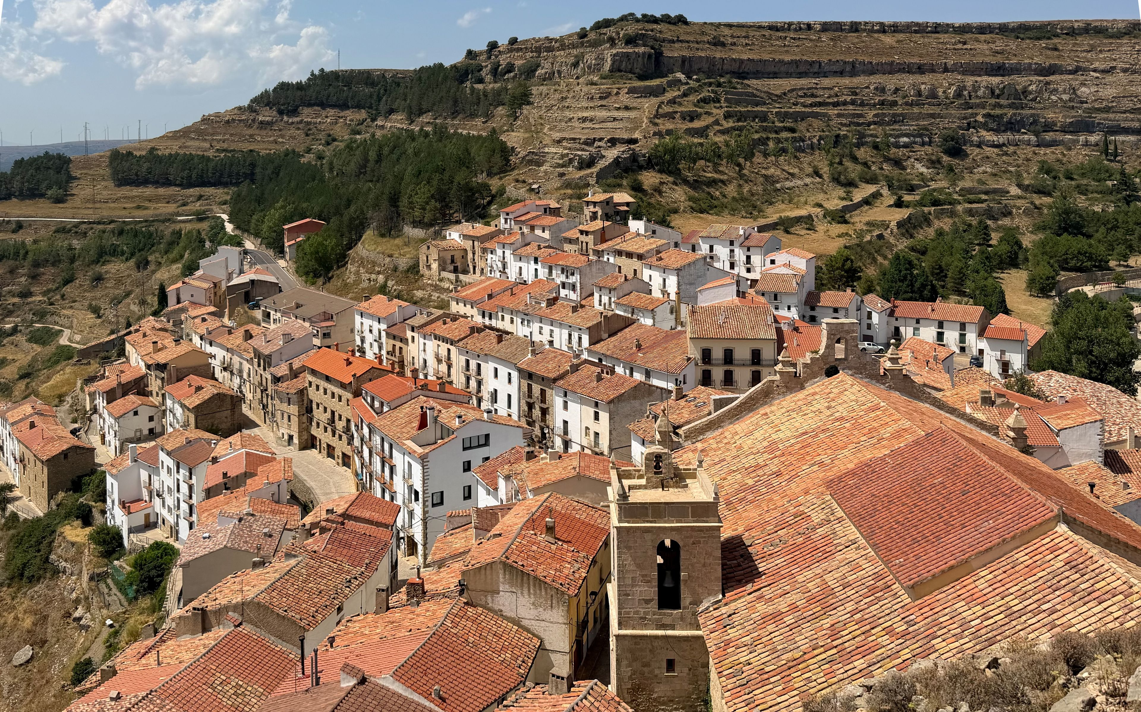A town with terracotta-roofed buildings nestled in a valley, surrounded by hills and sparse vegetation.