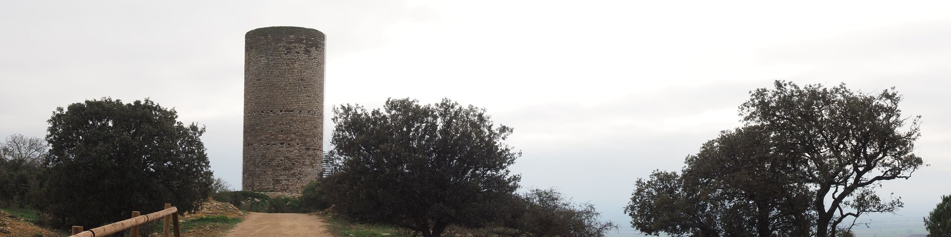 A stone tower on a dirt path with trees on either side.