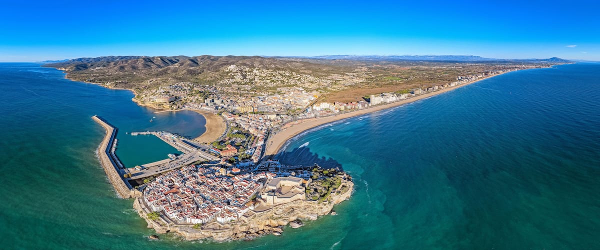 An aerial view of a coastal town with a prominent peninsula, a fortified castle, and a long beachfront.