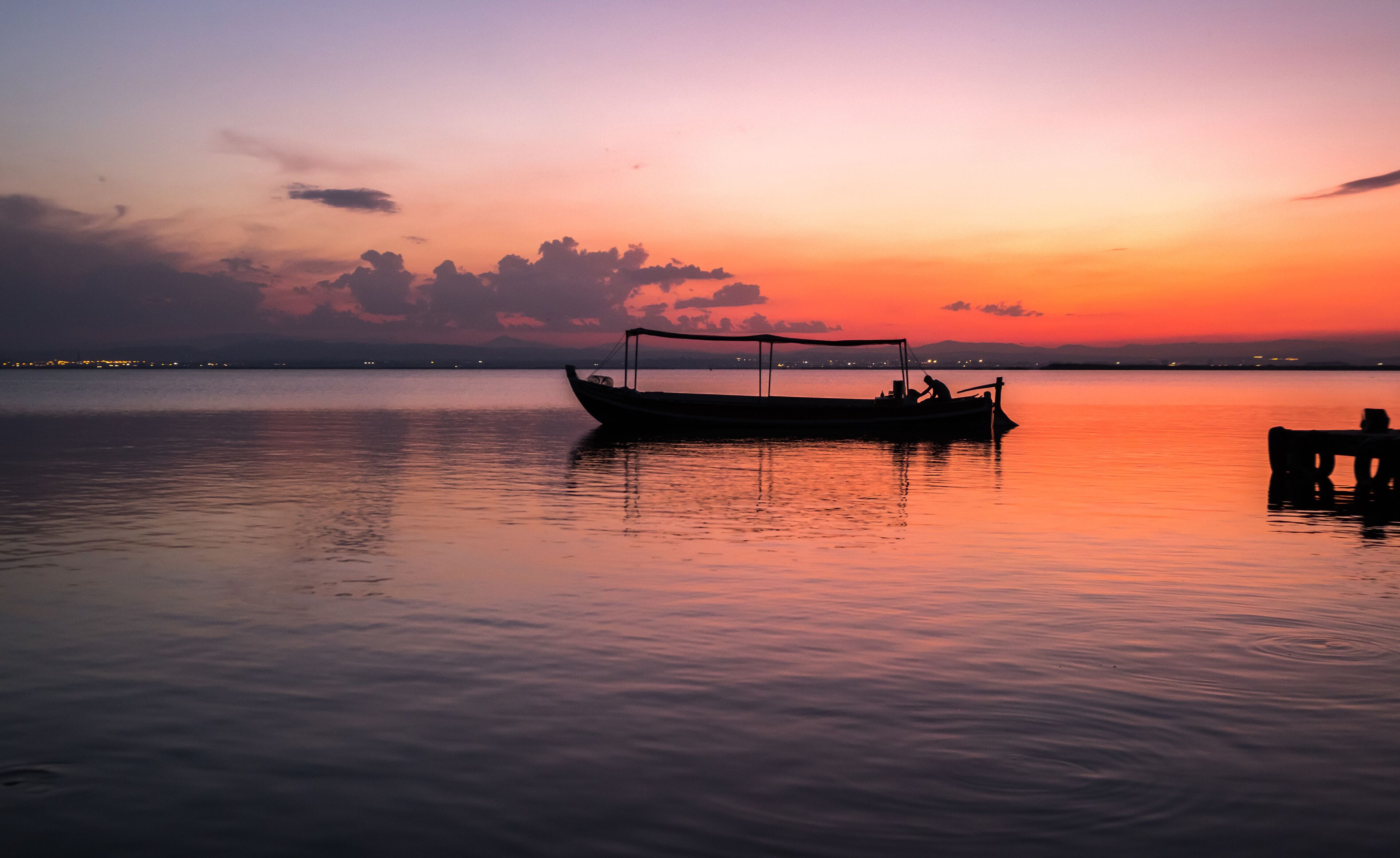 A boat on calm water during sunset with a city skyline in the background.