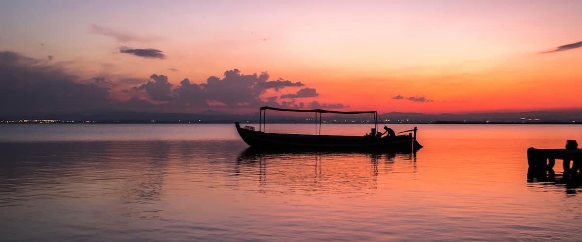 A boat on calm water during sunset with a city skyline in the background.