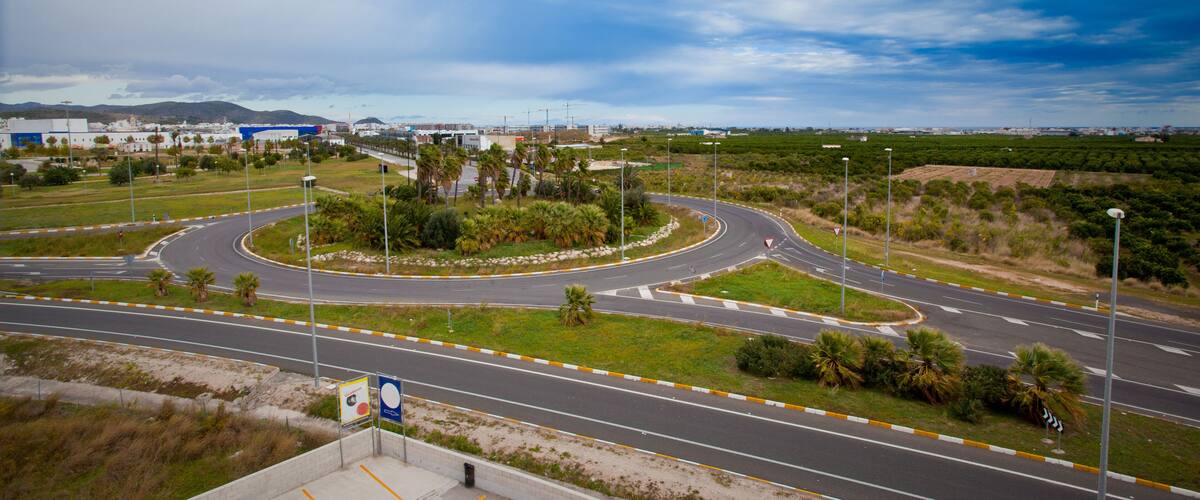 A roundabout with multiple exits, surrounded by greenery and palm trees, with buildings in the background.