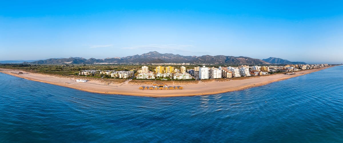 A coastal cityscape with a beach, buildings, and mountains in the background.