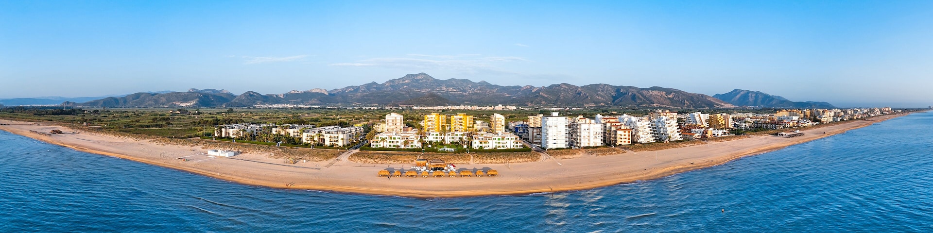 A coastal cityscape with a beach, buildings, and mountains in the background.