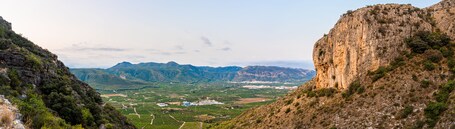 Eine gebirgige Landschaft mit Weinbergen und einer in der Ferne liegenden Stadt.