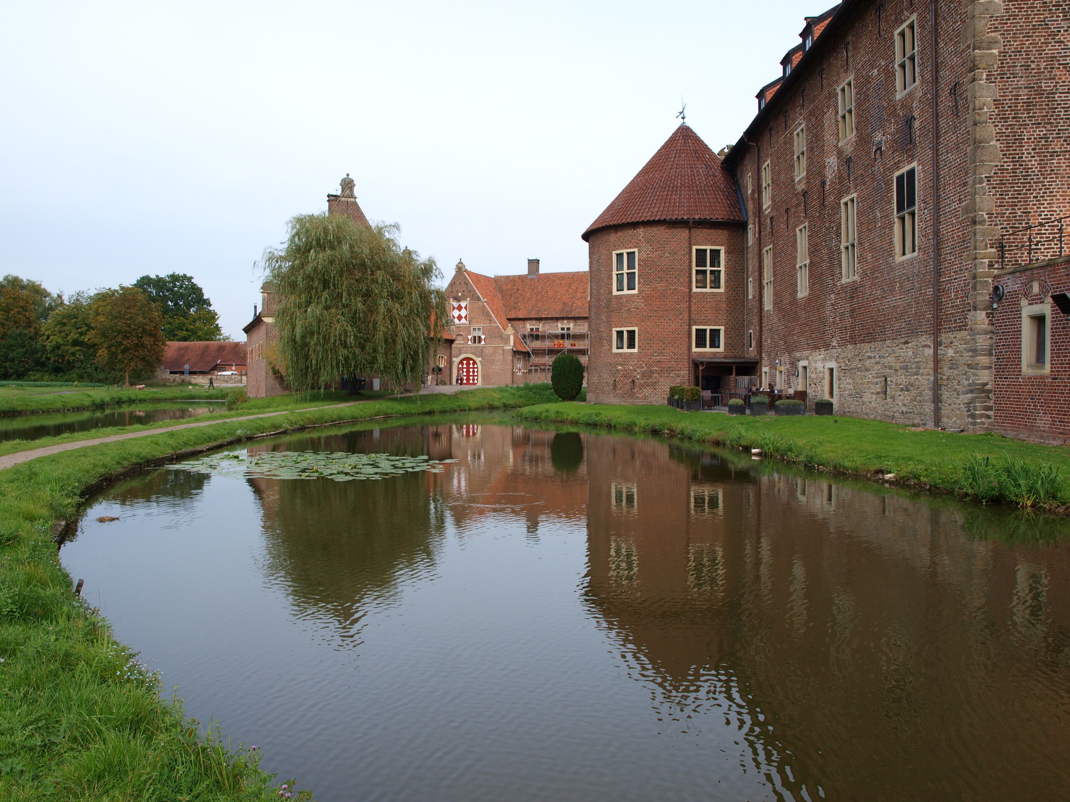 A canal with a reflection of a brick building and a tree.