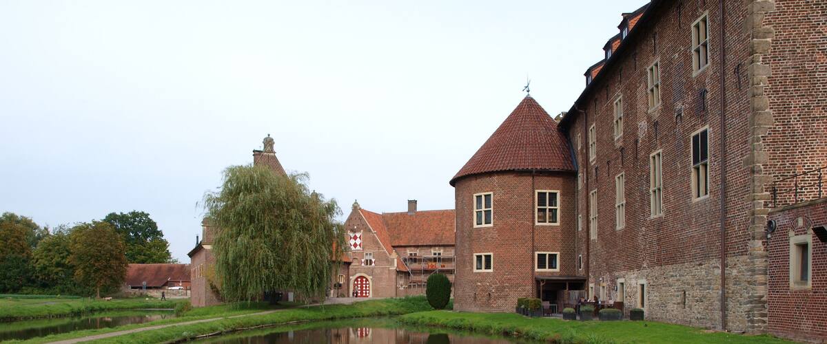 A canal with a reflection of a brick building and a tree.