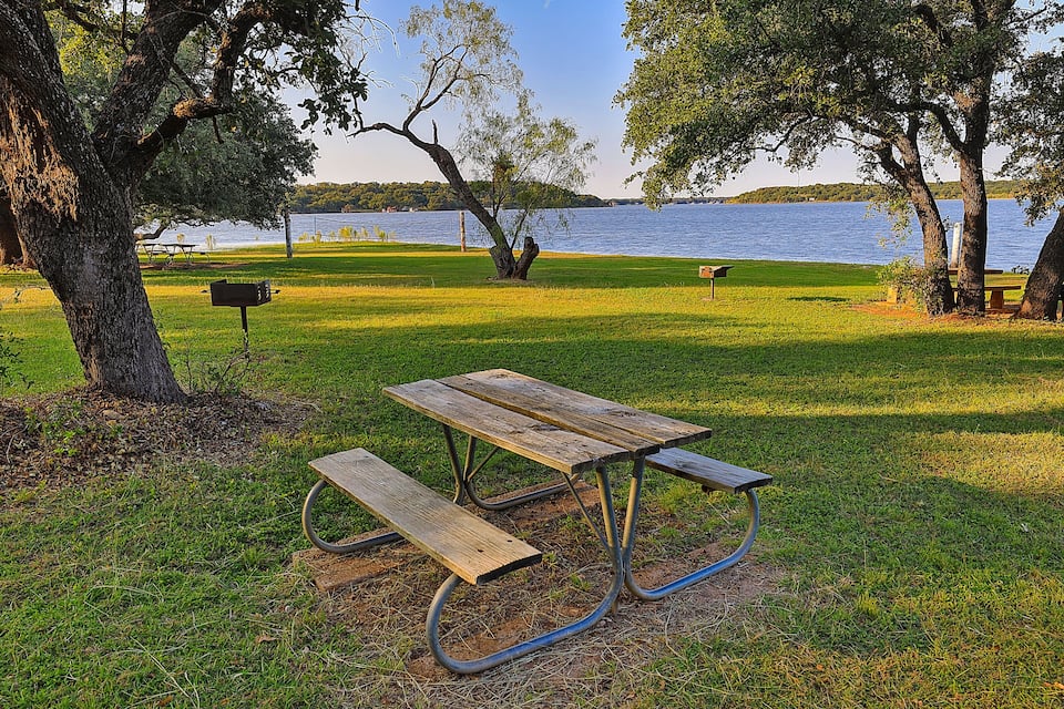 A picnic table in a grassy park with a lake in the background.