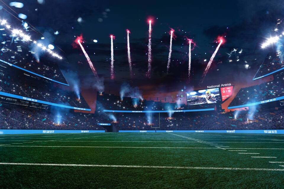 A stadium with a scoreboard, bright lights, and a crowd.
