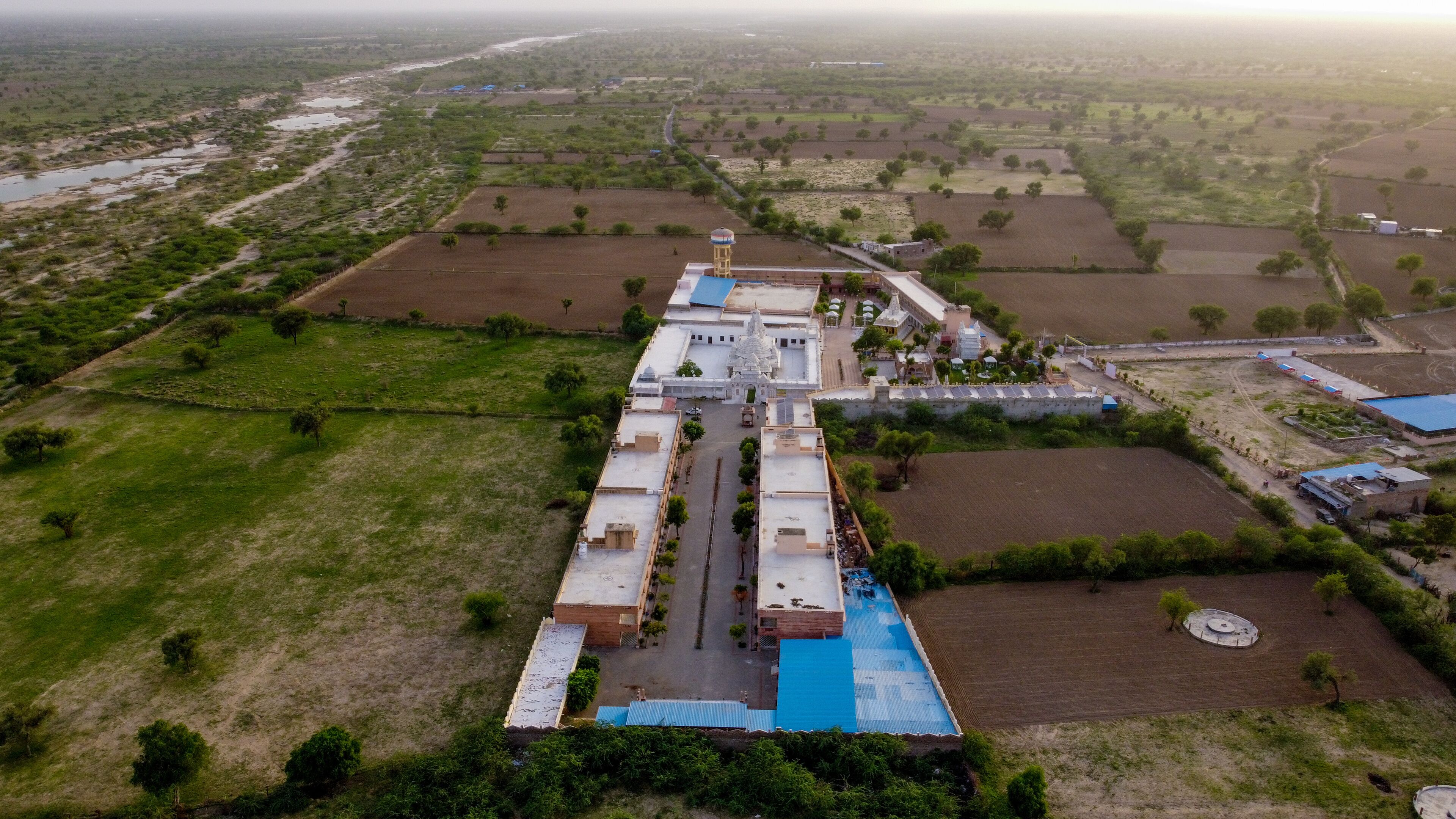 An aerial view of a large industrial complex with multiple buildings, surrounded by agricultural fields and a river.