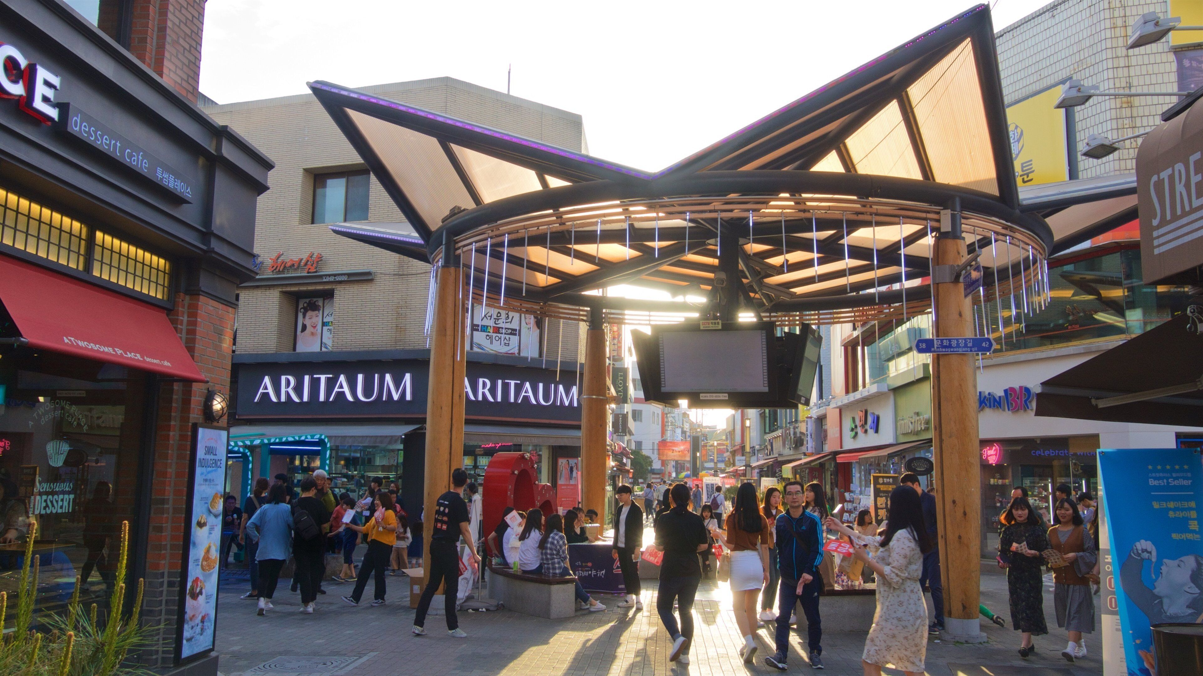A busy shopping area with a covered walkway, various shops, and people walking.