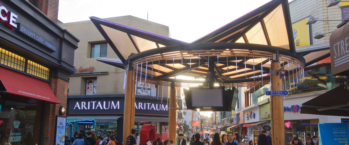 A busy shopping area with a covered walkway, various shops, and people walking.