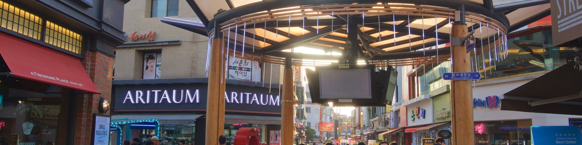A busy shopping area with a covered walkway, various shops, and people walking.