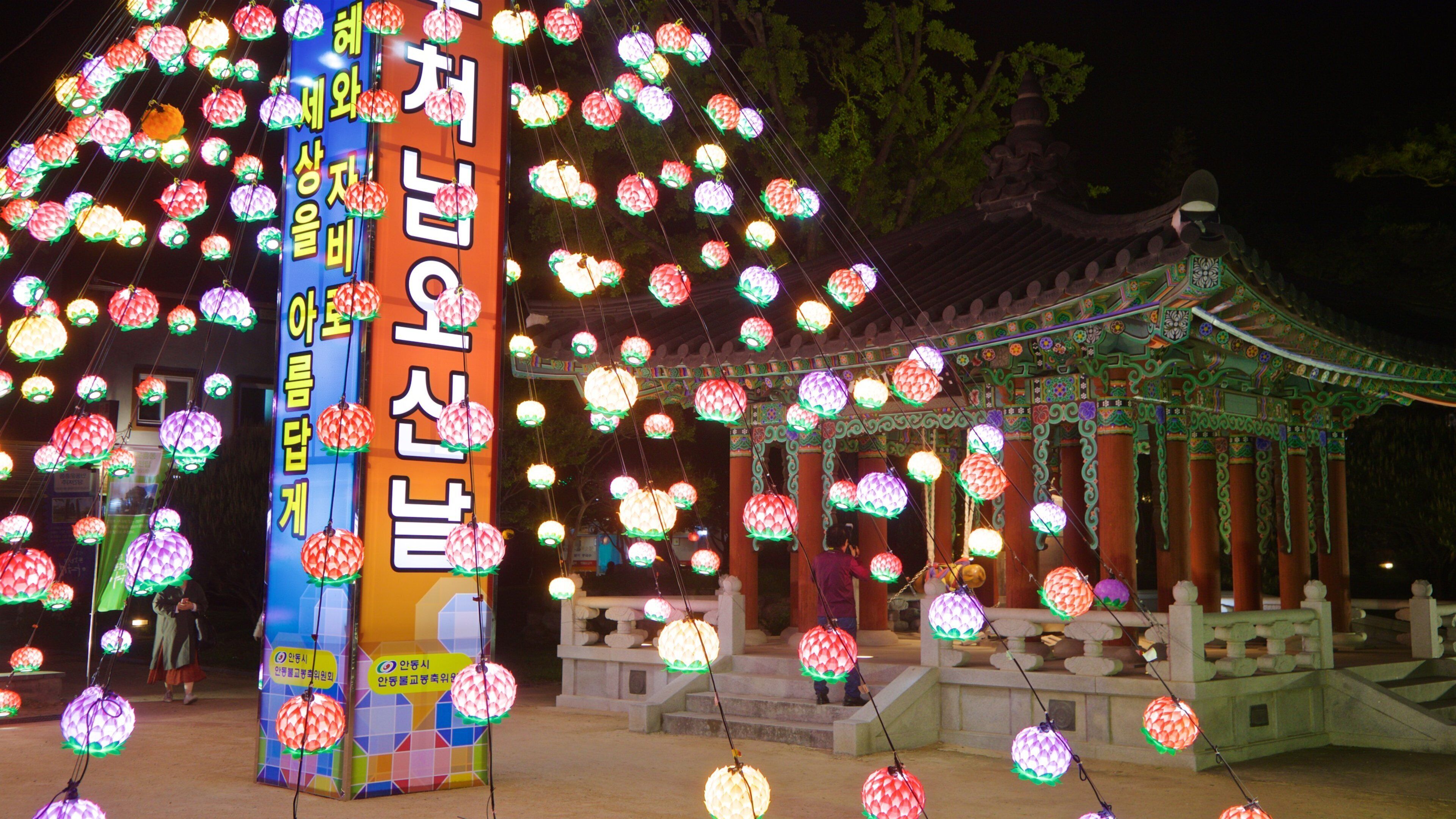 A traditional Korean pavilion with colorful lanterns and a large vertical sign with Korean text.
