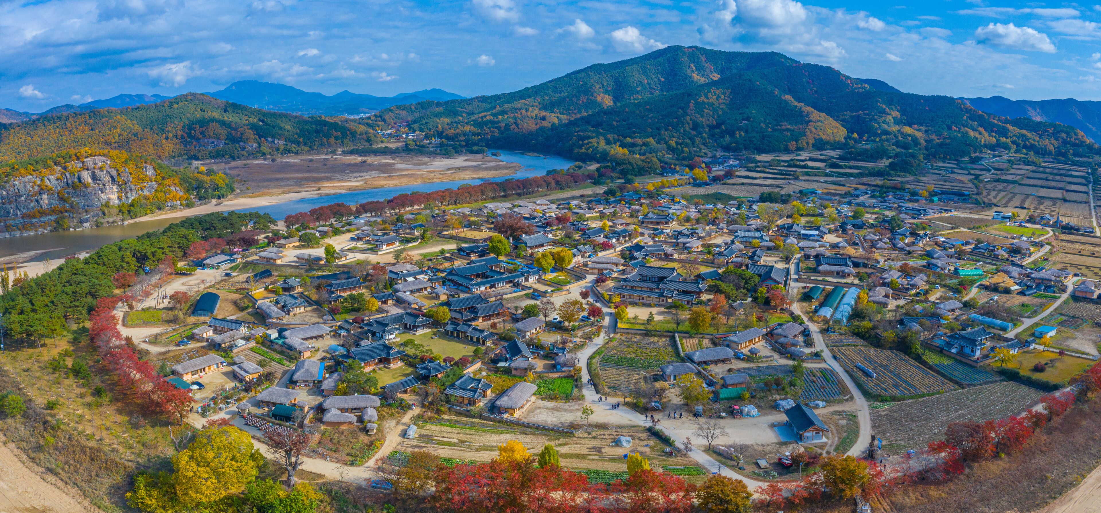 A mountainous town with traditional houses, a river, and autumn foliage.