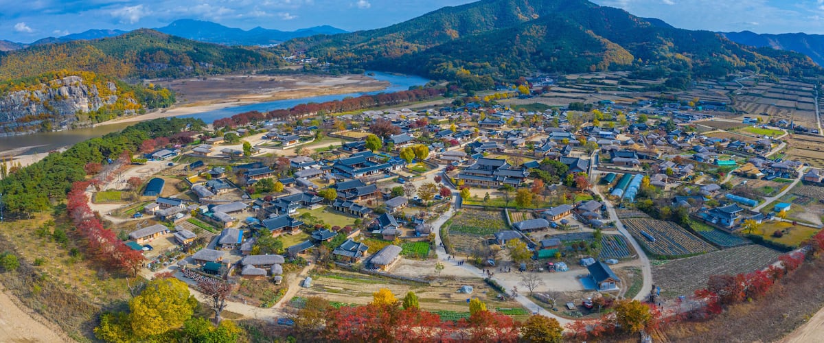 A mountainous town with traditional houses, a river, and autumn foliage.