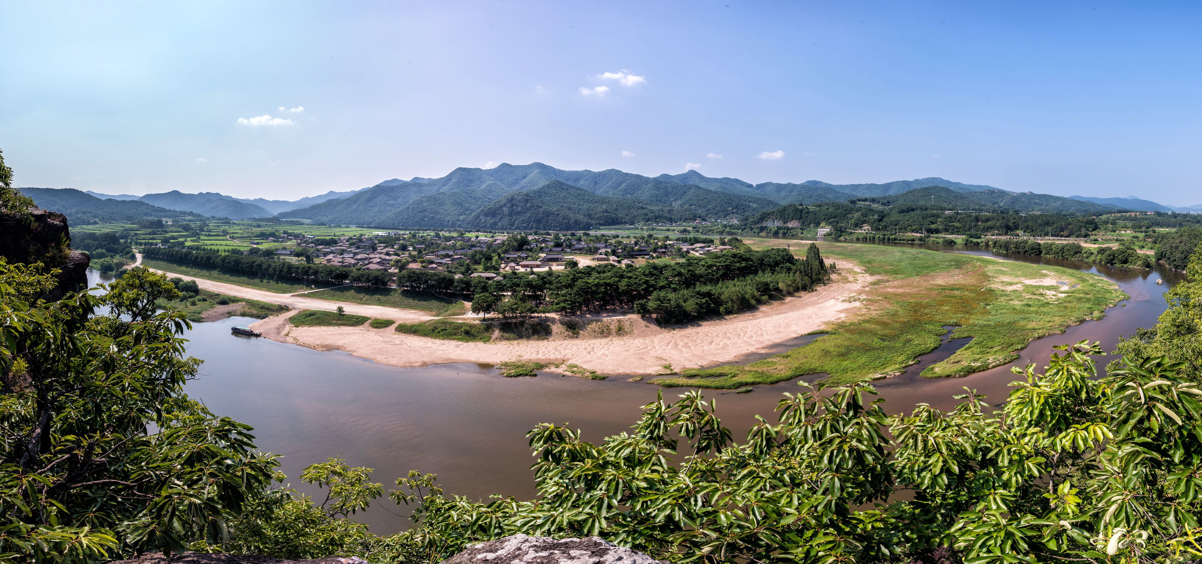 A river winding through a valley with mountains in the background and dense greenery along the riverbanks.