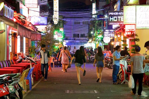 A busy street with neon signs, motorcycles, and people walking.