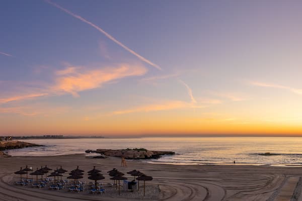 Uma praia com guarda-sóis, cadeiras e um pôr do sol.