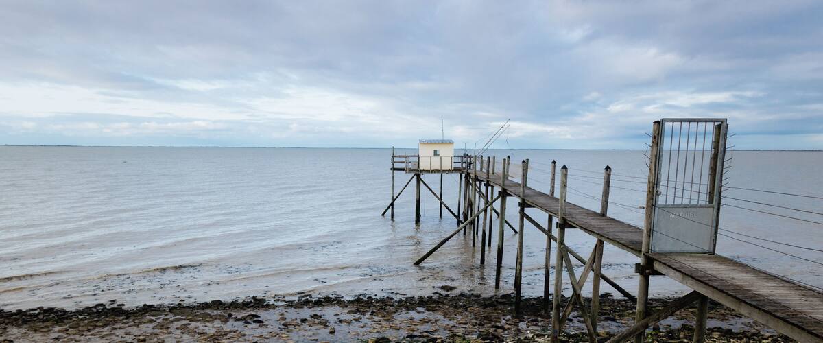 A wooden pier extending into calm waters with a small white building at the end.