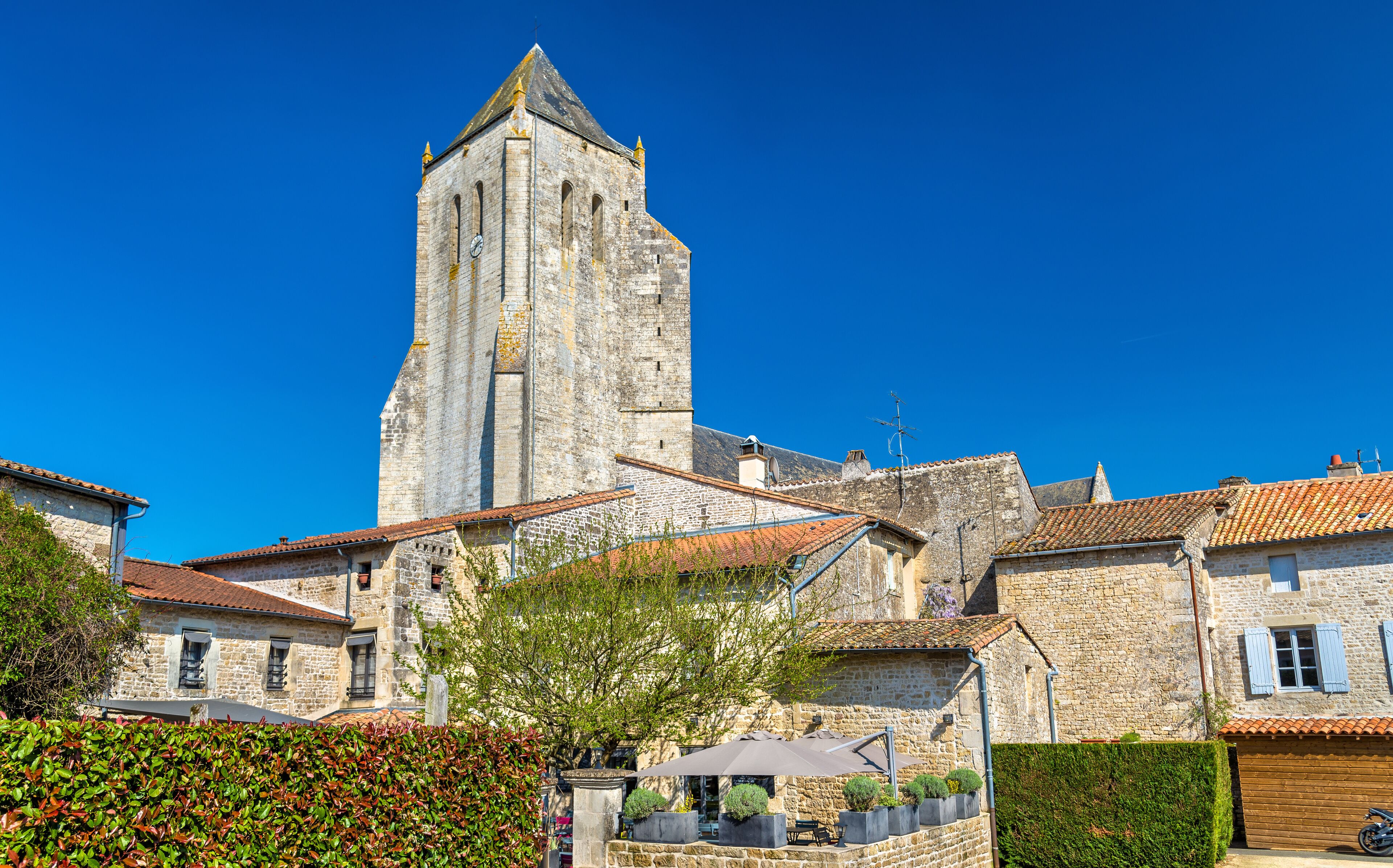 A historic stone tower with a clock, surrounded by traditional stone buildings with red-tiled roofs.