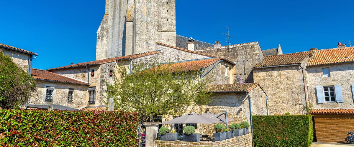 A historic stone tower with a clock, surrounded by traditional stone buildings with red-tiled roofs.