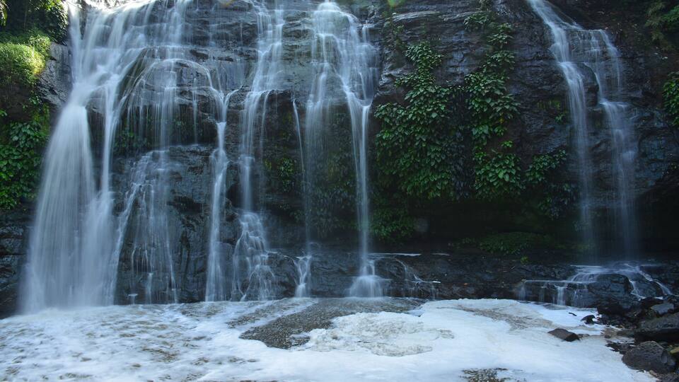 A waterfall cascading over a rocky cliff surrounded by lush greenery.