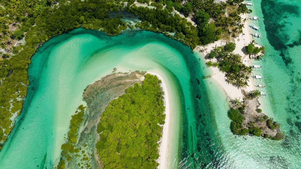 A tropical beach with clear turquoise waters, a white sandy shore, and lush green vegetation.