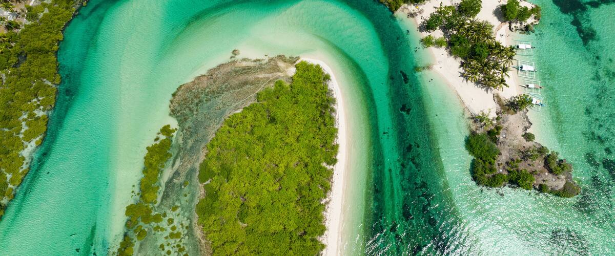 A tropical beach with clear turquoise waters, a white sandy shore, and lush green vegetation.