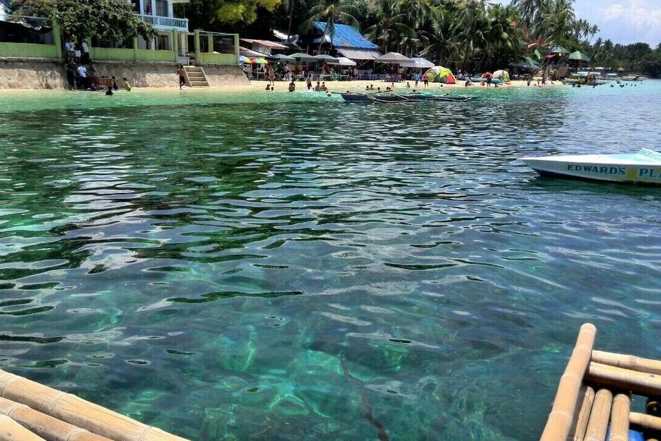 A clear tropical beach with a boat named 'EDWARDS PLAT' and a dock with wooden planks.