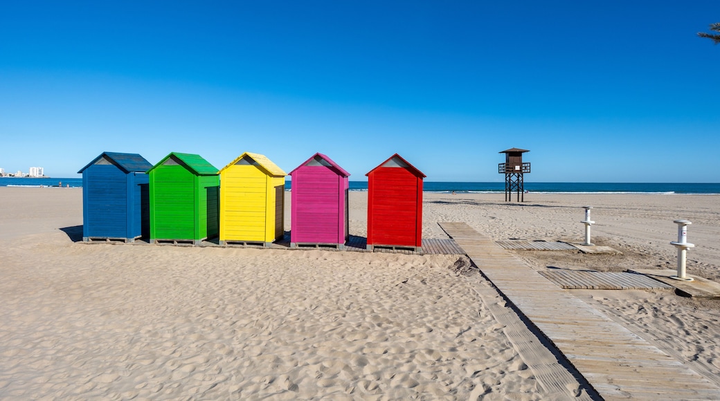 A row of colorful beach huts on a sandy beach with a clear blue sky.