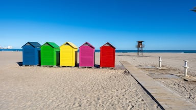 Una hilera de cabañas de playa coloridas en una playa arenosa con un cielo azul despejado.