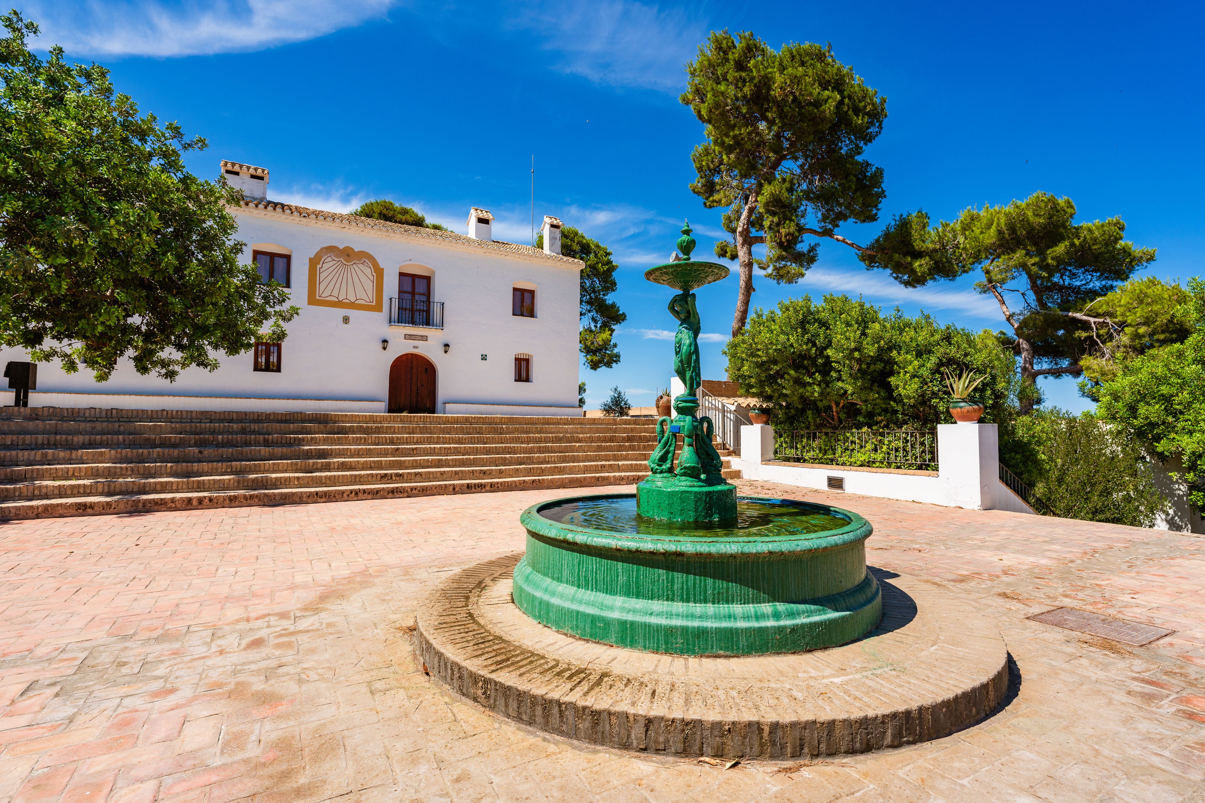 Une cour avec une fontaine, des marches menant à un bâtiment et des arbres.